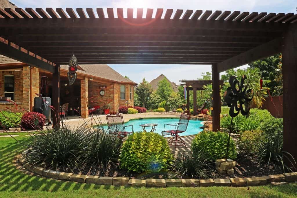 A backyard with a pergola, metal chairs, landscaped plants, and a swimming pool — outdoor living spaces by Ellis Landscape Services