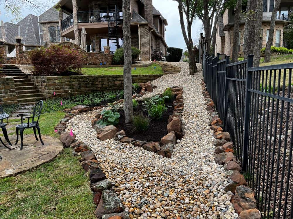 A stone-bordered drainage pathway in a landscaped backyard — drainage solutions by Ellis Landscape Services